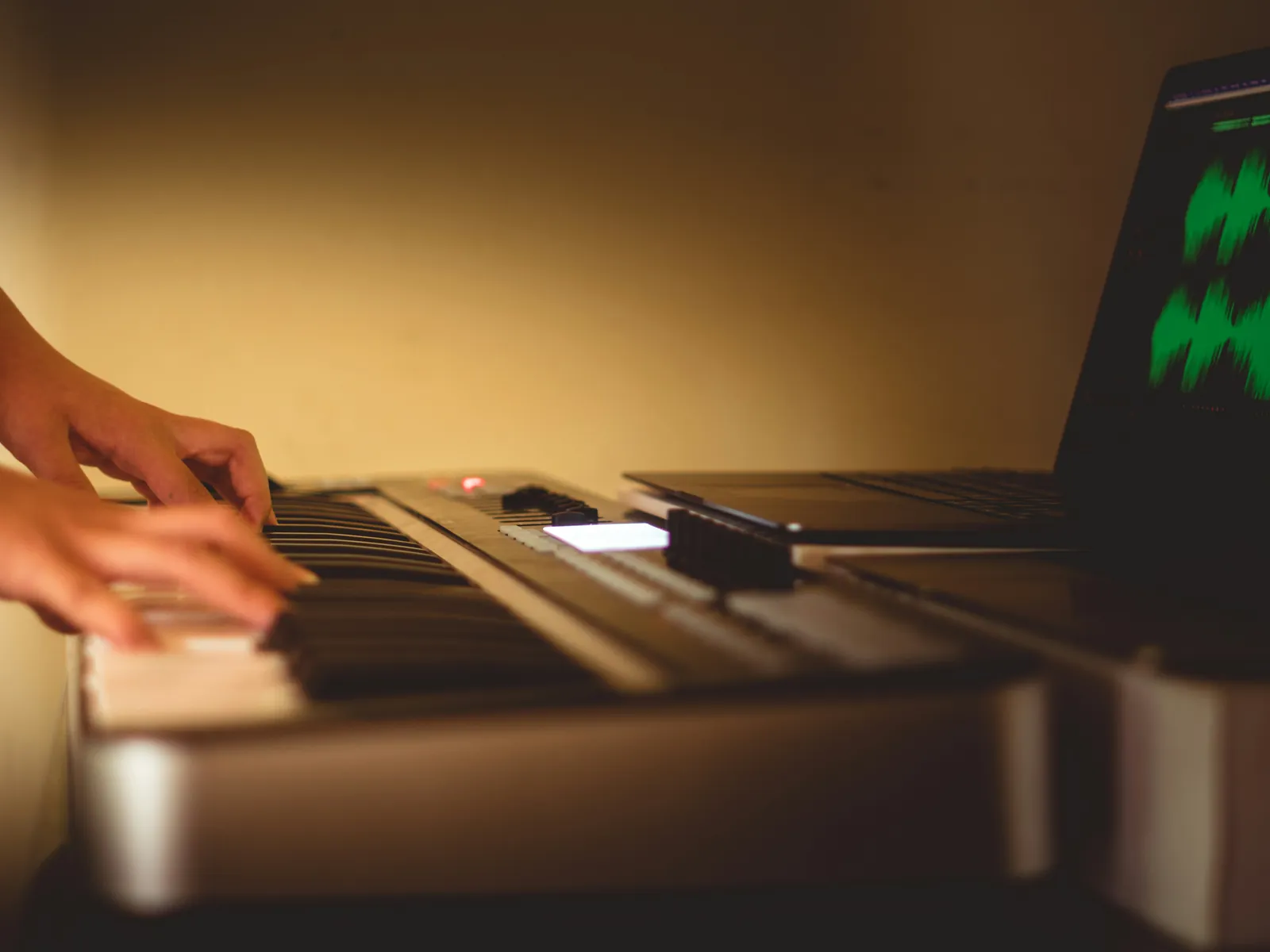 Le mani di una persona che suona una tastiera, con il portatile accanto